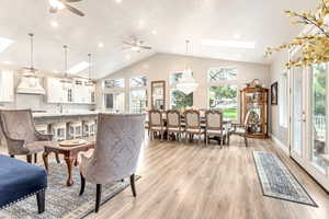 Dining space with a skylight, high vaulted ceiling, light wood-type flooring, and ceiling fan