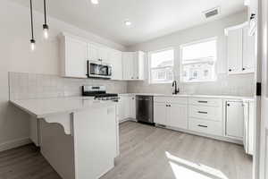 Kitchen with white cabinets, appliances with stainless steel finishes, sink, and pendant lighting