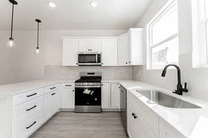 Kitchen featuring sink, hanging light fixtures, white cabinets, and stainless steel appliances