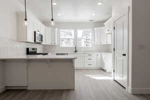 Kitchen featuring white cabinetry, kitchen peninsula, hanging light fixtures, stainless steel appliances, and a kitchen bar