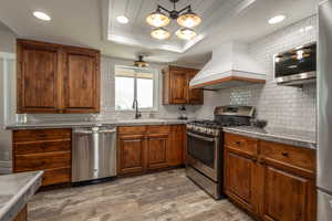 Kitchen with decorative backsplash, wood-type flooring, custom exhaust hood, and appliances with stainless steel finishes