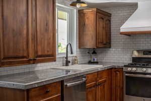 Kitchen with sink, decorative backsplash, appliances with stainless steel finishes, and premium range hood