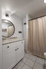 Bathroom featuring wooden walls, a textured ceiling, tile patterned floors, toilet, and vanity