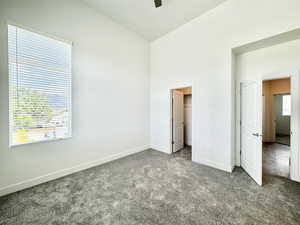 Unfurnished bedroom featuring dark colored carpet, multiple windows, and a walk in closet