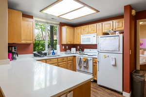 Kitchen featuring light brown cabinetry, sink, wood-type flooring, and white appliances