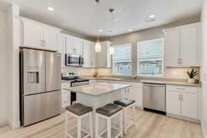 Kitchen with a kitchen island, light hardwood / wood-style floors, appliances with stainless steel finishes, pendant lighting, and sink