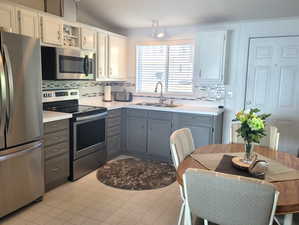 Kitchen with appliances with stainless steel finishes, light tile patterned floors, white cabinets, and sink