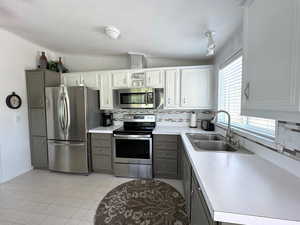 Kitchen featuring gray cabinetry, stainless steel appliances, vaulted ceiling, and light tile patterned floors