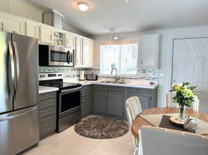 Kitchen with light tile patterned flooring, stainless steel appliances, white cabinets, sink, and gray cabinetry