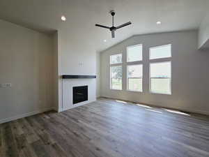 Unfurnished living room with lofted ceiling, wood-type flooring, a brick fireplace, and ceiling fan