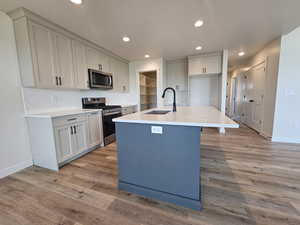 Kitchen with sink, a center island with sink, light hardwood / wood-style floors, appliances with stainless steel finishes, and backsplash