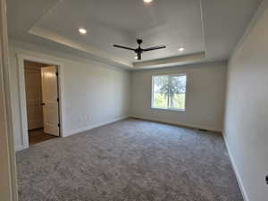 Carpeted empty room featuring ceiling fan and a tray ceiling