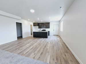 Kitchen with dark brown cabinetry, sink, light hardwood / wood-style flooring, and a center island with sink