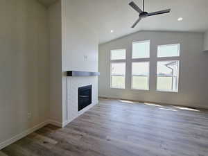 Unfurnished living room with ceiling fan, a fireplace, hardwood / wood-style flooring, and lofted ceiling