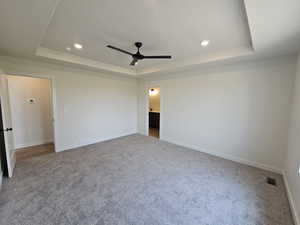 Unfurnished bedroom featuring ceiling fan, carpet, and a tray ceiling