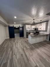 Kitchen featuring a peninsula, dark countertops, a notable chandelier, a barn door, and appliances with stainless steel finishes