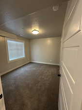 Empty room with baseboards, dark colored carpet, and a textured ceiling