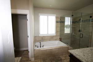 Bathroom featuring a stall shower, vanity, a garden tub, and baseboards