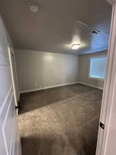 Unfurnished bedroom featuring a textured ceiling, baseboards, visible vents, and dark carpet