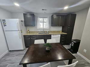 Kitchen featuring white appliances, light stone counters, light hardwood / wood-style flooring, and sink