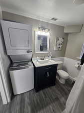 Bathroom featuring hardwood / wood-style floors, a textured ceiling, stacked washer / drying machine, toilet, and vanity