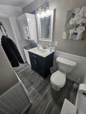 Bathroom with vanity, stacked washer and dryer, toilet, and hardwood / wood-style flooring