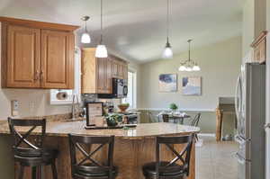 Kitchen with appliances with stainless steel finishes, vaulted ceiling, sink, pendant lighting, and light tile patterned floors