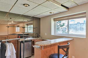 Kitchen with kitchen peninsula, a drop ceiling, a breakfast bar area, and light stone counters