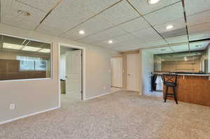 Interior space featuring a paneled ceiling, carpet floors, and bar