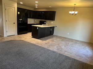 Kitchen with dark brown cabinets, black appliances, light colored carpet, pendant lighting, and sink