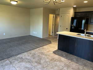 Kitchen featuring an inviting chandelier, sink, light colored carpet, dark brown cabinetry, and black fridge with ice dispenser