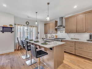 Kitchen with light hardwood / wood-style flooring, tasteful backsplash, wall chimney range hood, hanging light fixtures, and sink