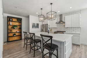 Kitchen with a center island with sink, light hardwood / wood-style flooring, stainless steel refrigerator with ice dispenser, and wall chimney range hood