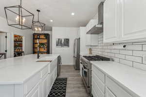 Kitchen featuring light wood-type flooring, wall chimney range hood, an island with sink, appliances with stainless steel finishes, and decorative backsplash