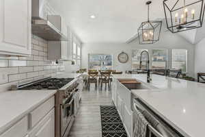 Kitchen featuring appliances with stainless steel finishes, a healthy amount of sunlight, light hardwood / wood-style floors, backsplash, and wall chimney exhaust hood