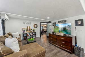 Living room with dark wood-type flooring, a wall unit AC, and a textured ceiling