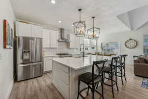 Kitchen with a center island with sink, light hardwood / wood-style floors, wall chimney exhaust hood, and stainless steel refrigerator with ice dispenser