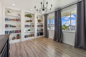 Sitting room with built in shelves, an inviting chandelier, and light wood-type flooring