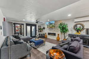 Living room with a stone fireplace, an AC wall unit, wood-type flooring, and ceiling fan