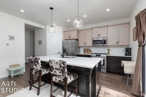 Kitchen featuring a kitchen island with sink, stainless steel appliances, hardwood / wood-style floors, decorative backsplash, and pendant lighting