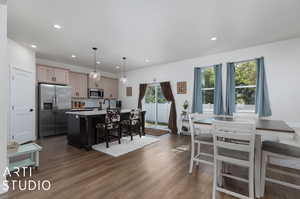 Kitchen with stainless steel appliances , decorative light fixtures, a kitchen breakfast bar, an island with sink, and dark hardwood / wood-style flooring