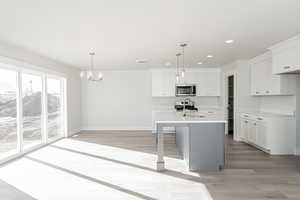 Kitchen featuring sink, a kitchen island with sink, stainless steel appliances, white cabinets, and decorative light fixtures