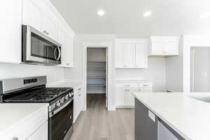 Kitchen with stainless steel appliances, light stone countertops, light hardwood / wood-style flooring, and white cabinets