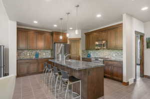 Kitchen featuring tile patterned flooring, stainless steel appliances, backsplash, and an island with sink