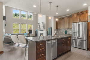 Kitchen featuring tile patterned floors, sink, dark stone countertops, appliances with stainless steel finishes, and a kitchen island with sink