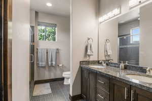 Bathroom featuring a shower with shower door, double vanity, tile patterned flooring, a textured ceiling, and toilet