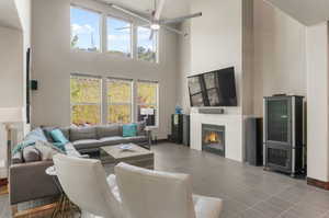 Living room featuring tile patterned floors, a tiled fireplace, ceiling fan, and a towering ceiling