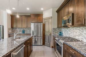 Kitchen featuring premium appliances, light tile patterned flooring, tasteful backsplash, decorative light fixtures, and sink