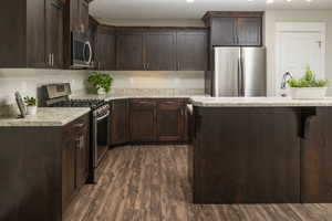 Kitchen featuring dark brown cabinets, light stone counters, dark hardwood / wood-style flooring, and appliances with stainless steel finishes