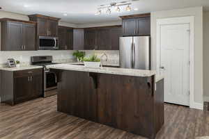 Kitchen featuring appliances with stainless steel finishes, dark brown cabinets, a center island, and dark wood-type flooring